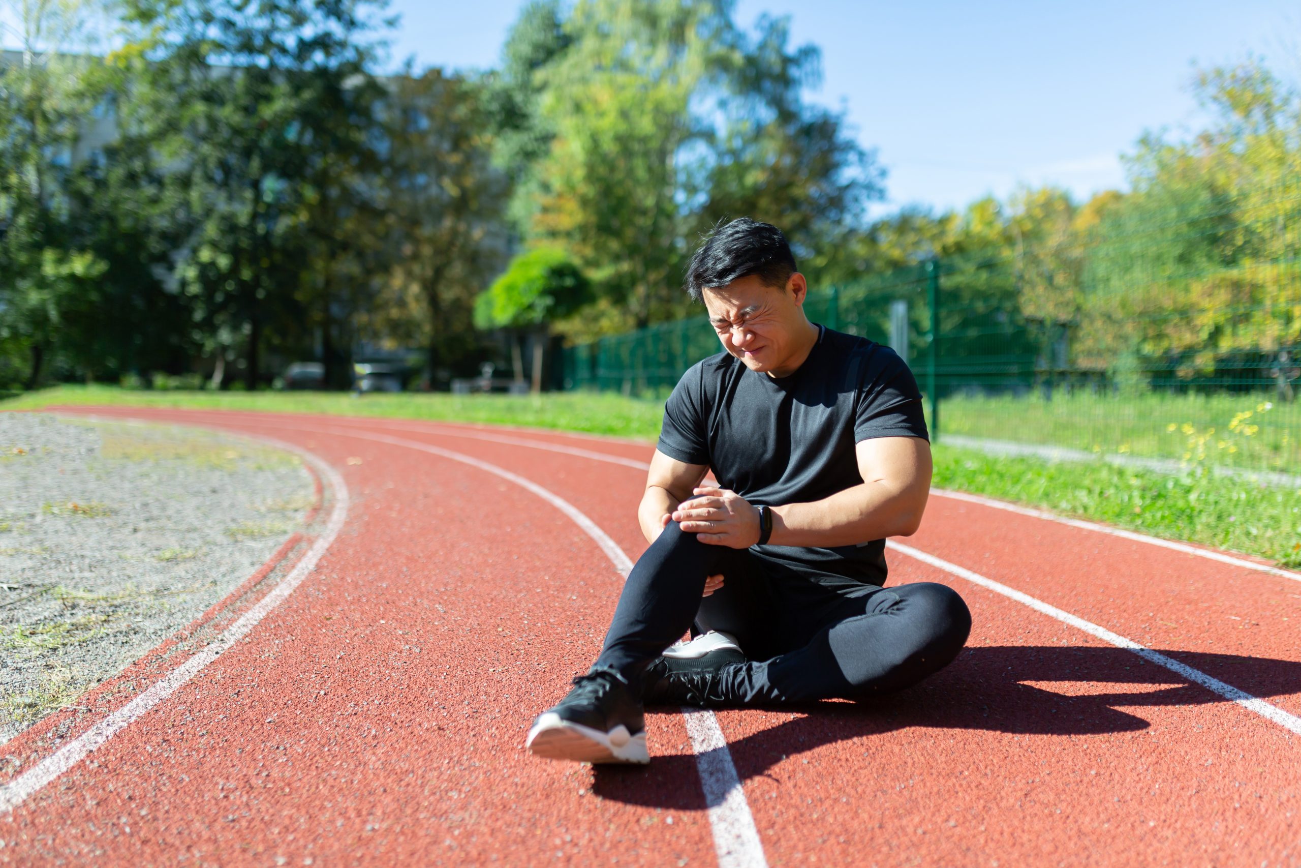 Sports injury at the stadium. A young Asian man is sitting on a treadm, holding his leg and knee
