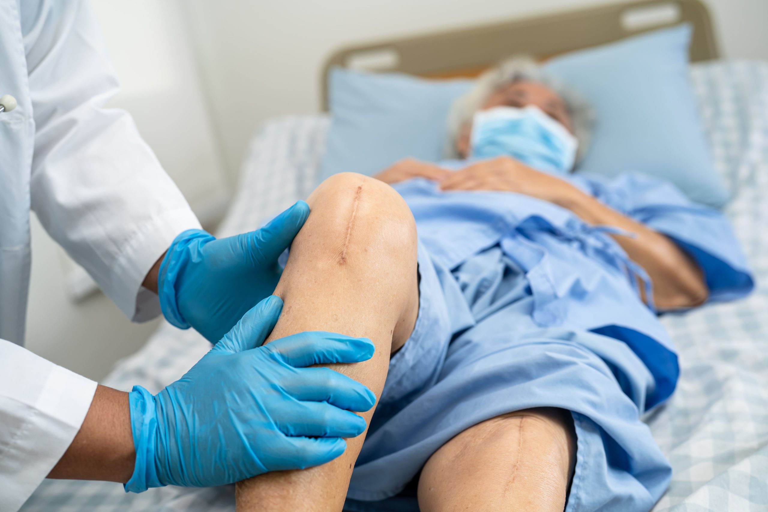 A doctor in gloves examining a senior patient's knee following surgery.