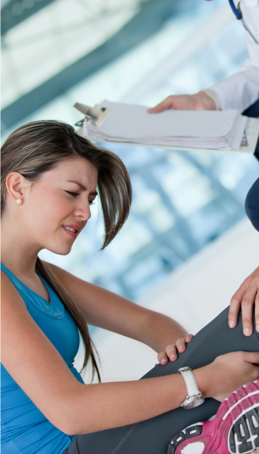 A woman in a blue athletic top is experiencing discomfort while a doctor examines her injured leg.