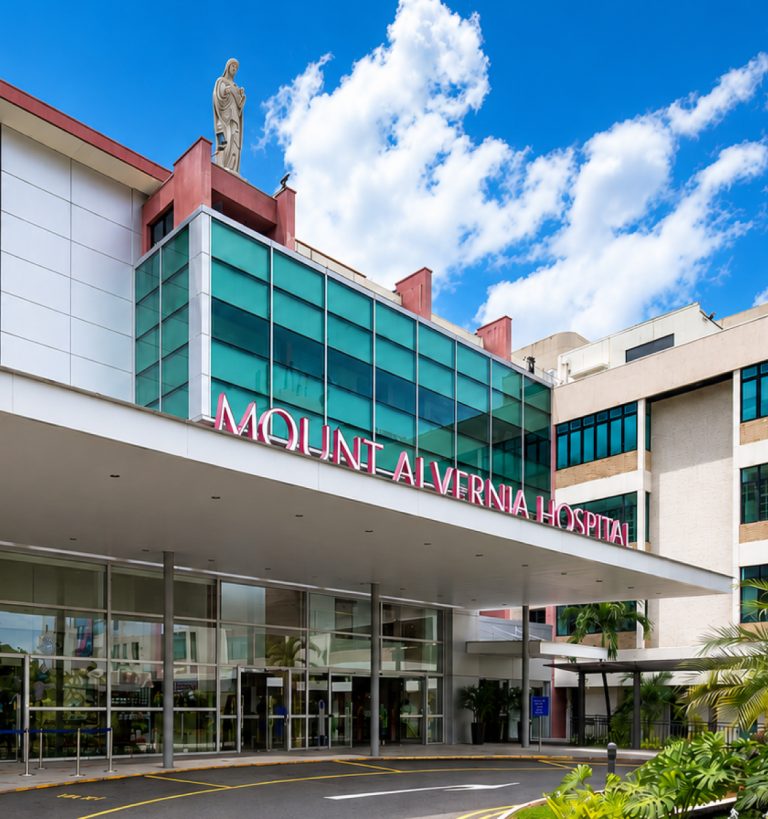 The entrance of Mount Alvernia Hospital with a statue above the building and a clear blue sky.